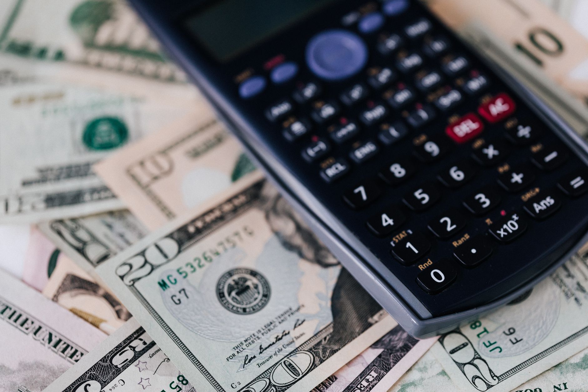 Photo: From above of electronic calculator placed over American cash paper money for budget planning and income and expenses calculation