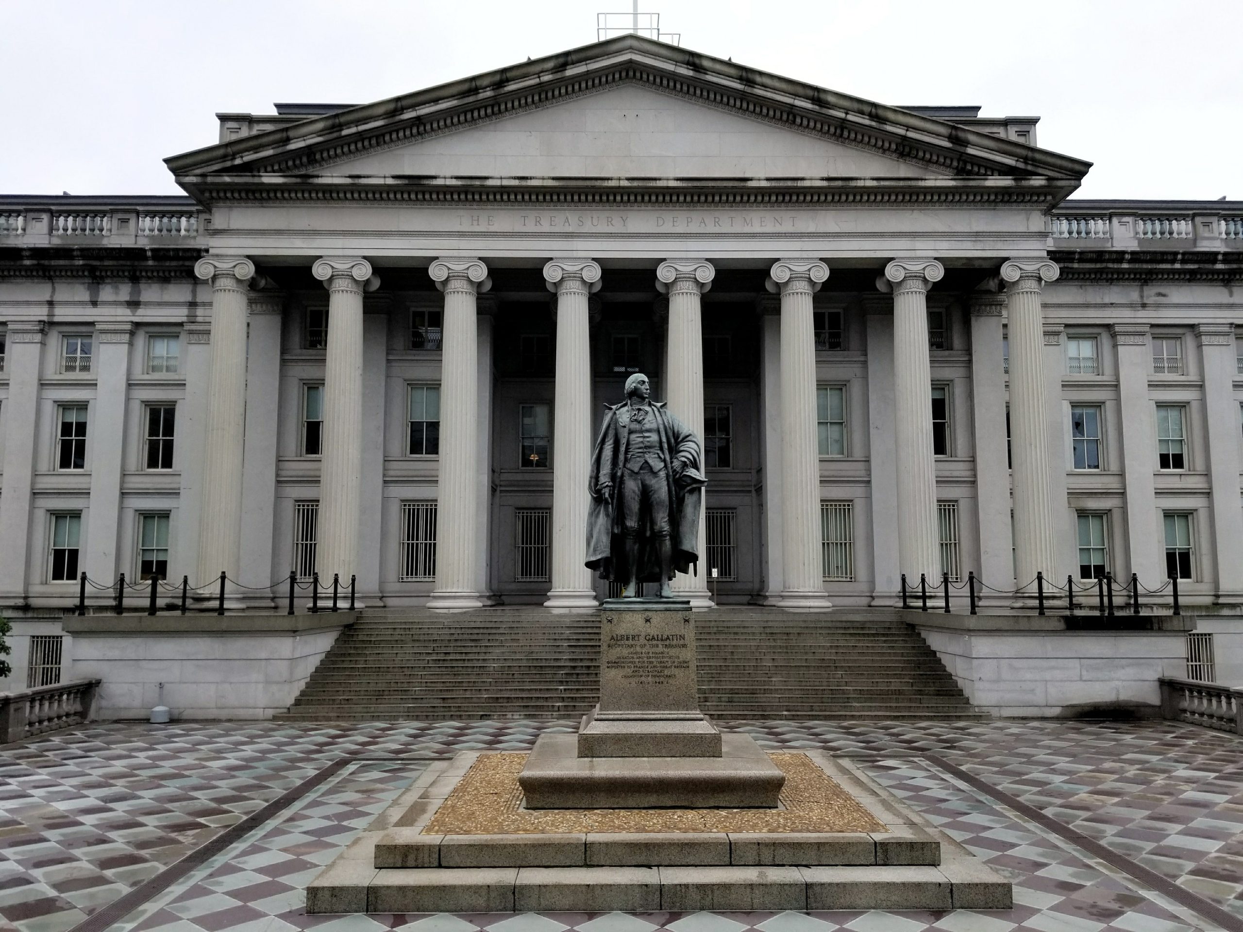 The columned north front of the U.S. Treasury Department building in Washington, inscribed "The Treasury Department," with the statue of Albert Gallatin in front.