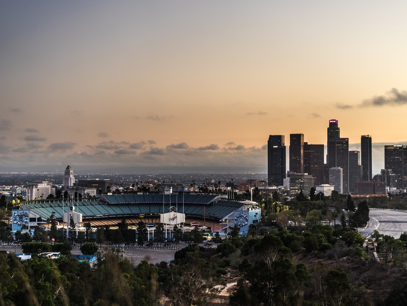 Dodger Stadium at dusk with the Downtown Los Angeles skyline and an orange sky behind it.