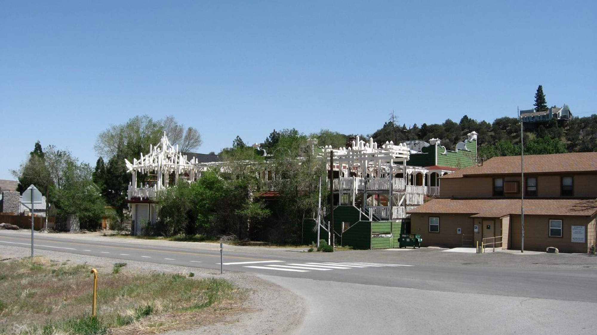 A road through the small town of Verdi, Nevada, with white wooden porch structures and a low brown building under a clear blue sky.