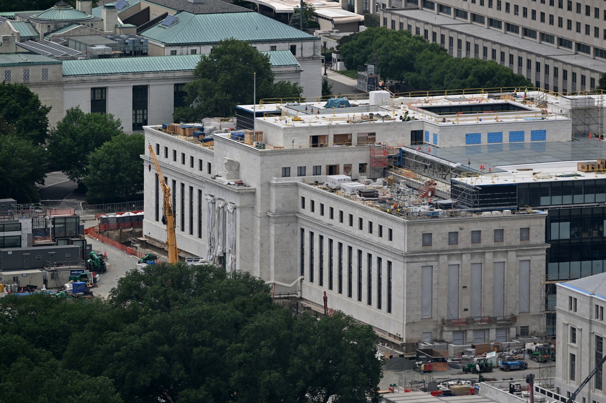 The Federal Reserve's Marriner S. Eccles building in Washington seen from above during its renovation, with a yellow crane, scaffolding and equipment on the roof and a fenced construction yard.