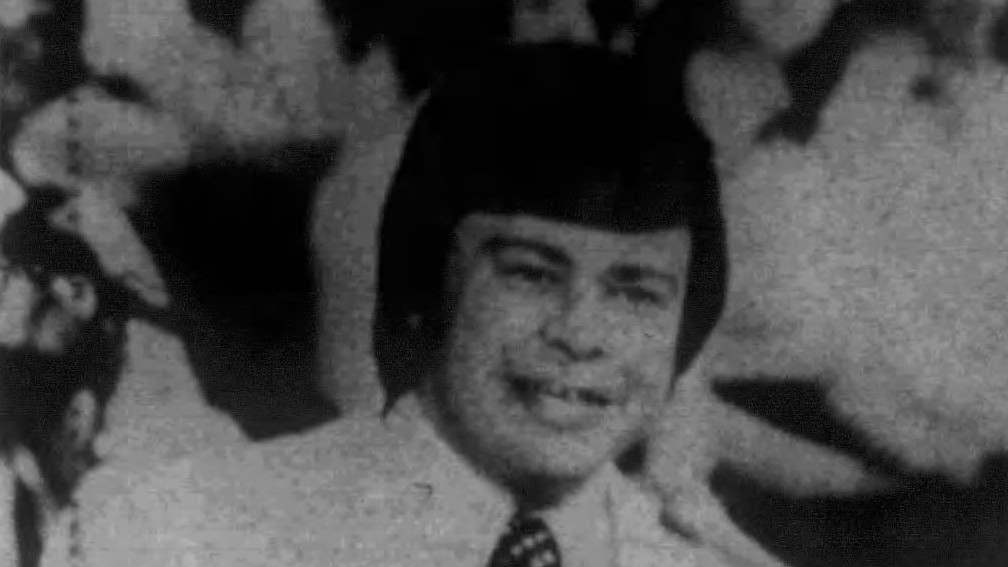 A black-and-white 1975 newspaper photograph of a young man with dark bowl-cut hair, a light jacket and a patterned tie, smiling, identified as Jim Bakker.
