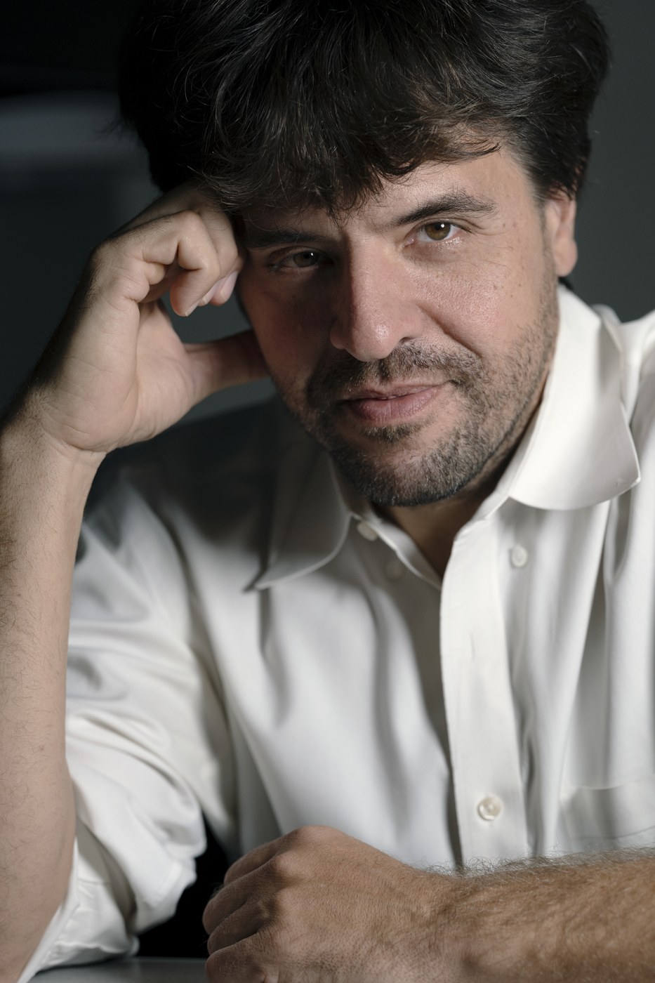 Portrait of Karl Deisseroth, a dark-haired man with a beard in a white shirt, resting his head on one hand.