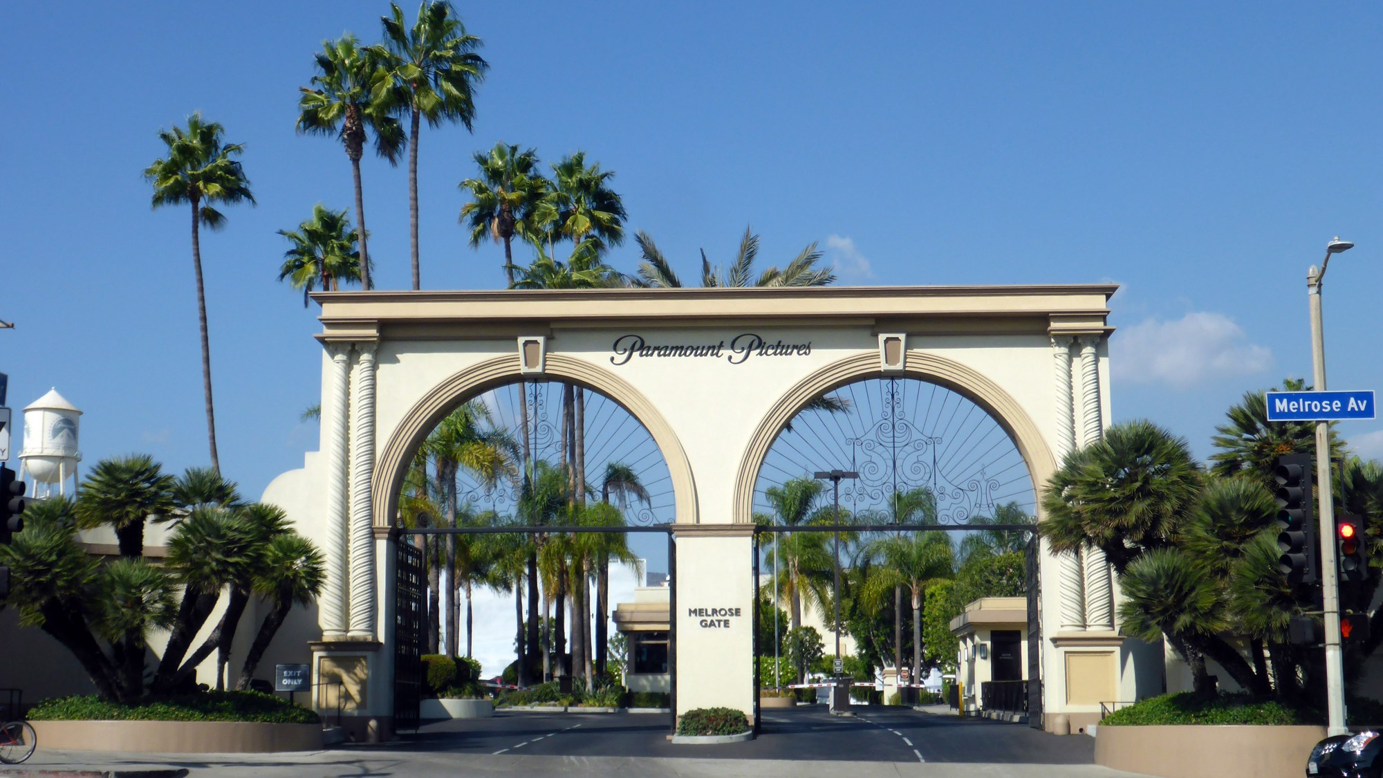 The arched Melrose Gate entrance to the Paramount Pictures studio lot in Los Angeles, with palm trees and a blue sky.