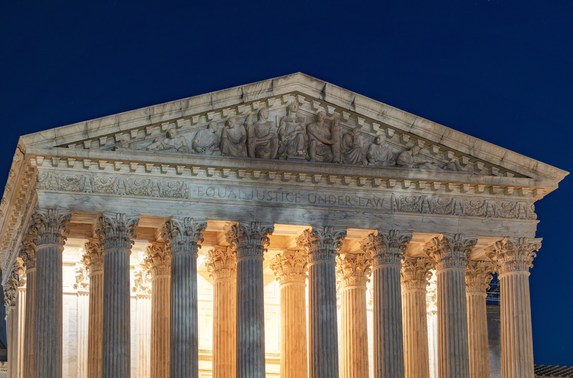 The west pediment and columns of the U.S. Supreme Court building in Washington lit at night, with the words Equal Justice Under Law carved above the columns.