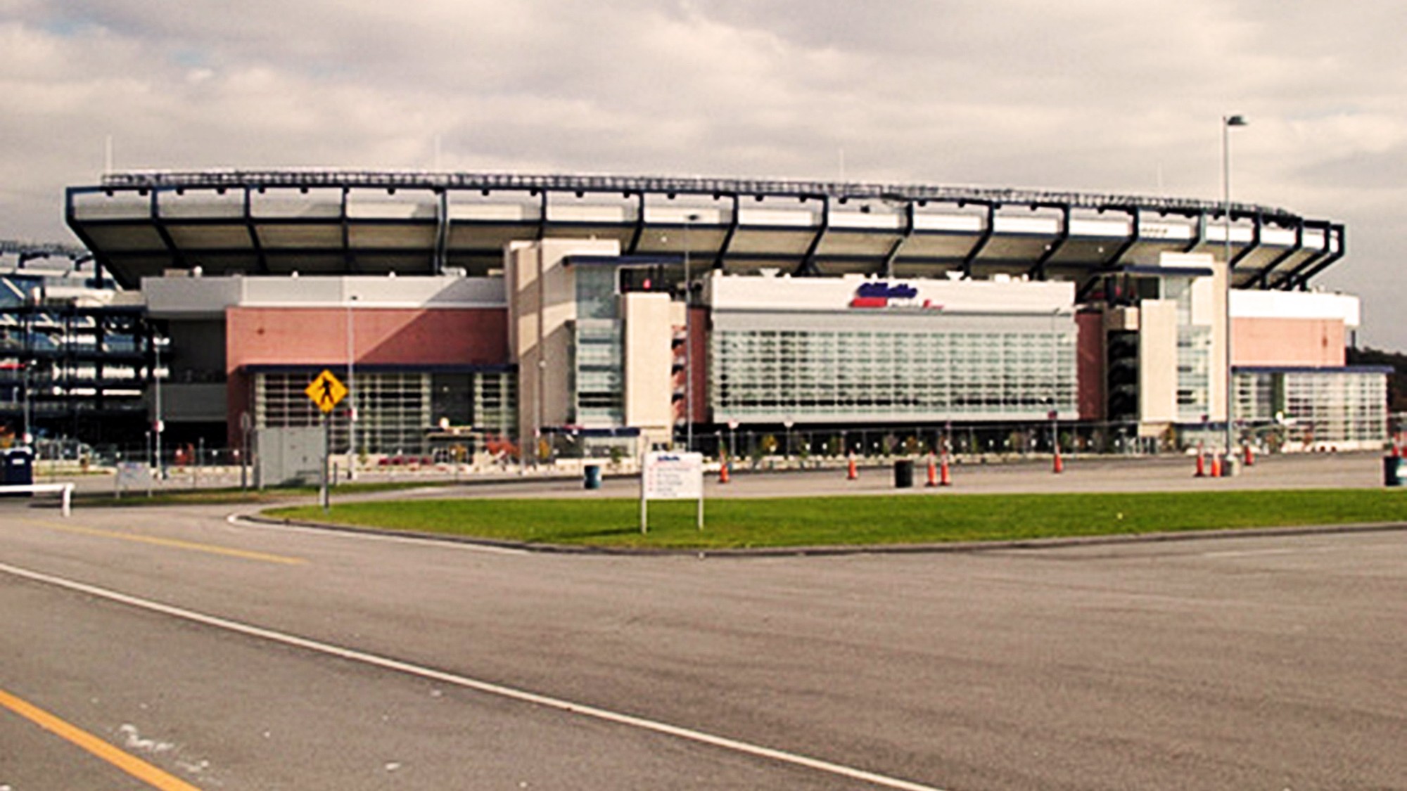 The exterior of Gillette Stadium in Foxborough, Massachusetts, seen from across an empty road under a cloudy sky.